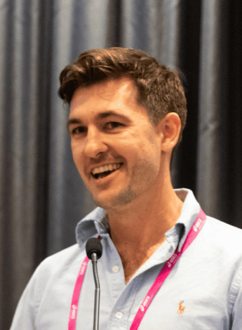 The image is of physiotherapist Daniel Hug giving a talk at a conference. 